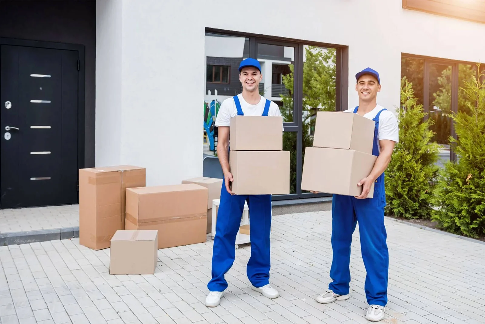 Two uniformed movers carrying stacked cartons out of a modern house
