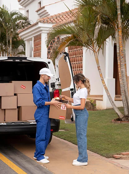 Mover handing a carton to a customer beside a loaded van outside a house