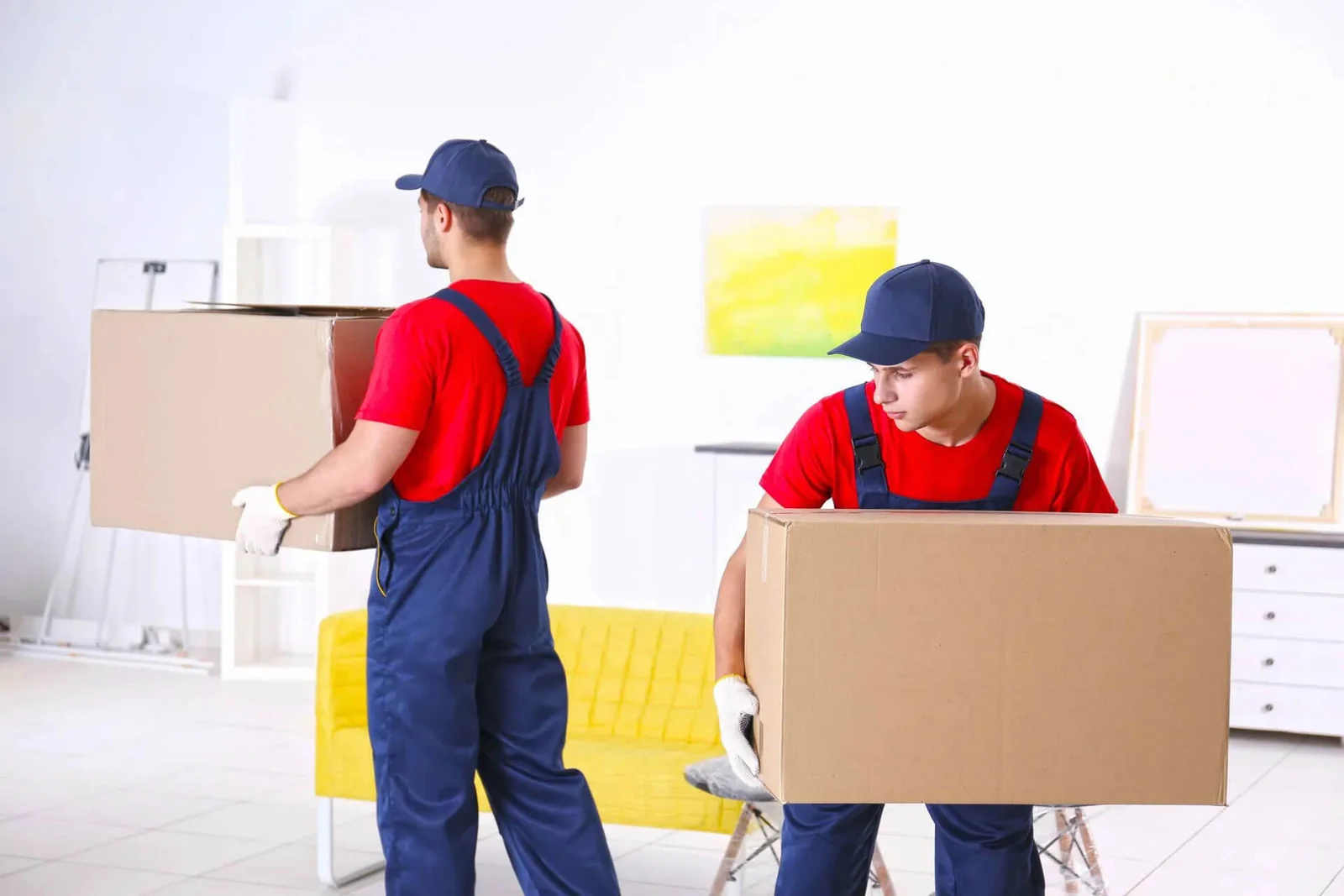 Movers carrying furniture and a large carton through a bright living room